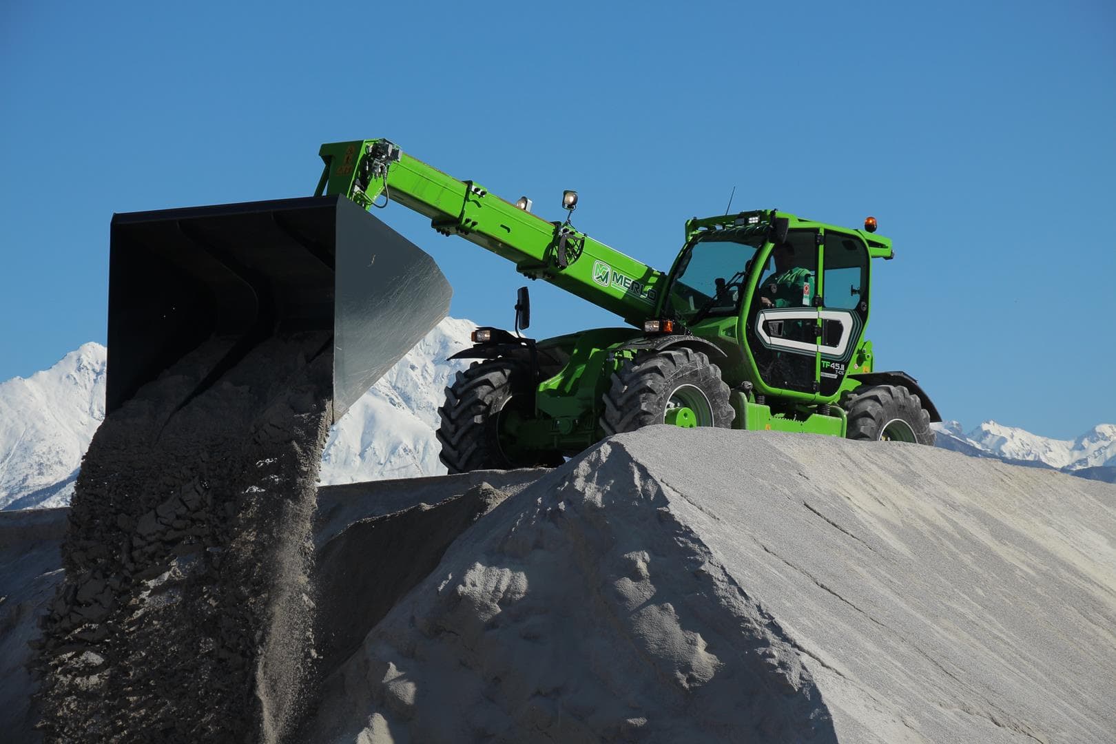 Merlo Turbofarmer 45.11 verreiker stort grondstoffen uit schepbak tegen bergachtige achtergrond.