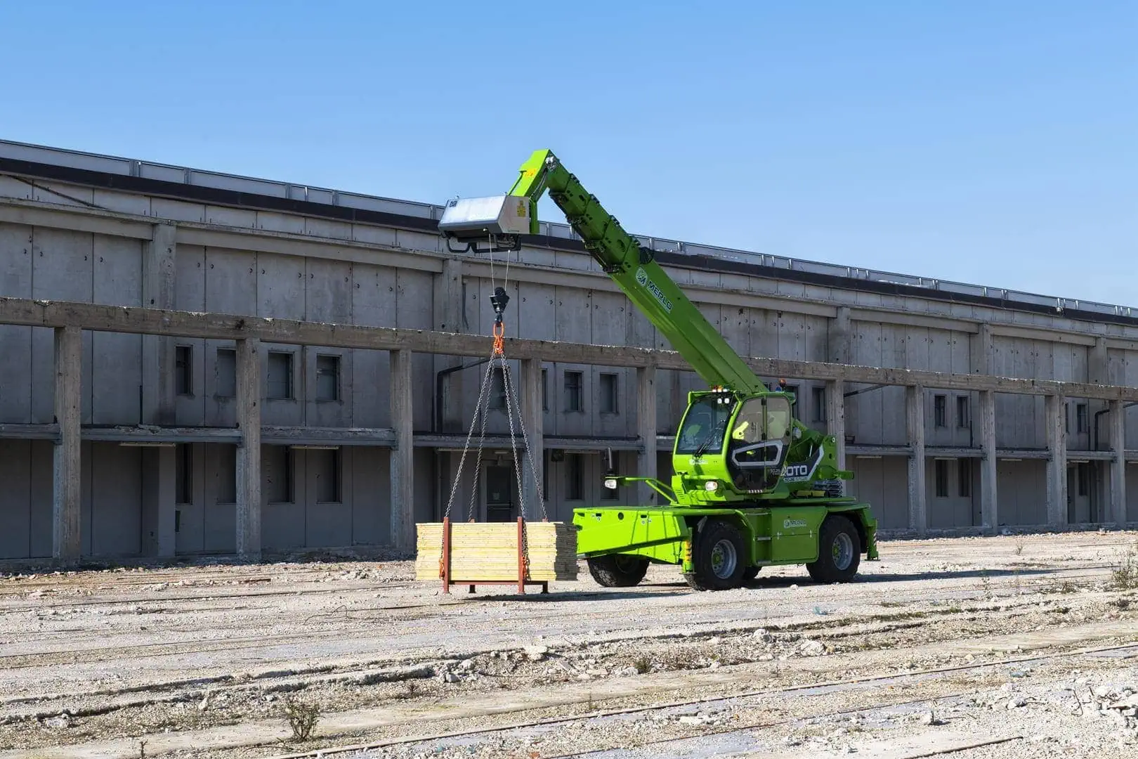 Merlo ROTO 50.21 roterende verreiker tilt een pallet op een bouwterrein.