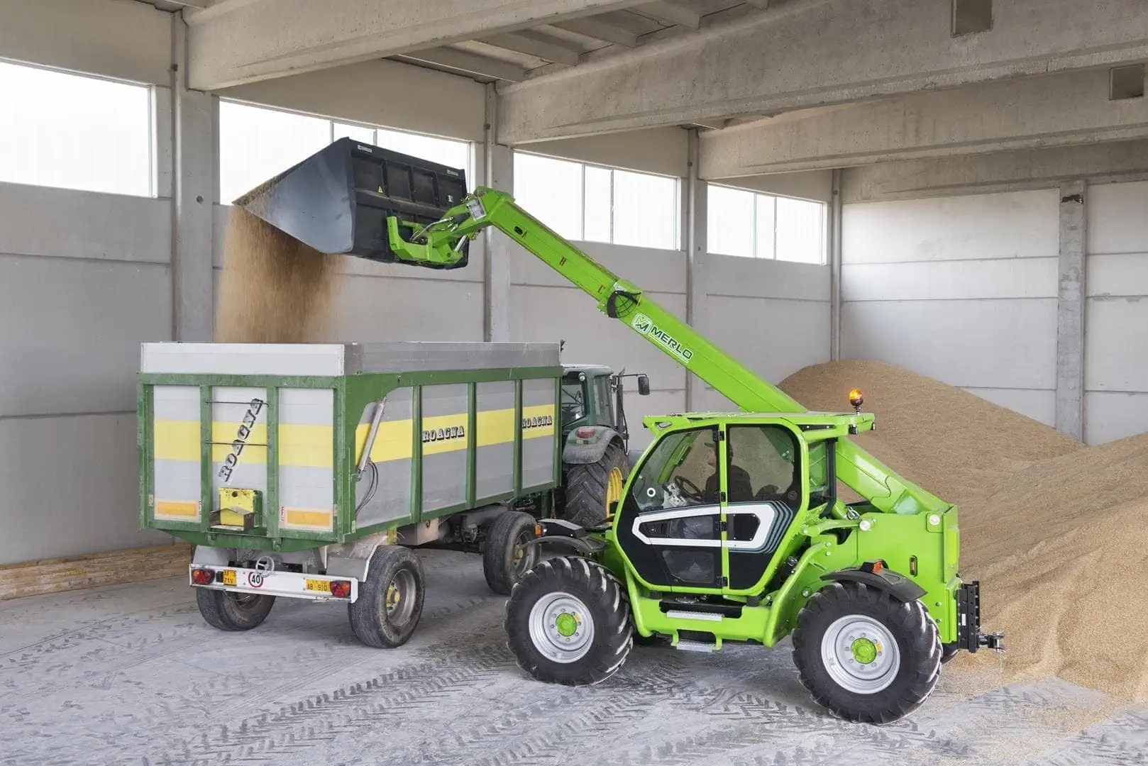 Merlo Turbofarmer 42.7 verreiker laadt materiaal in aanhangwagen in opslagruimte.