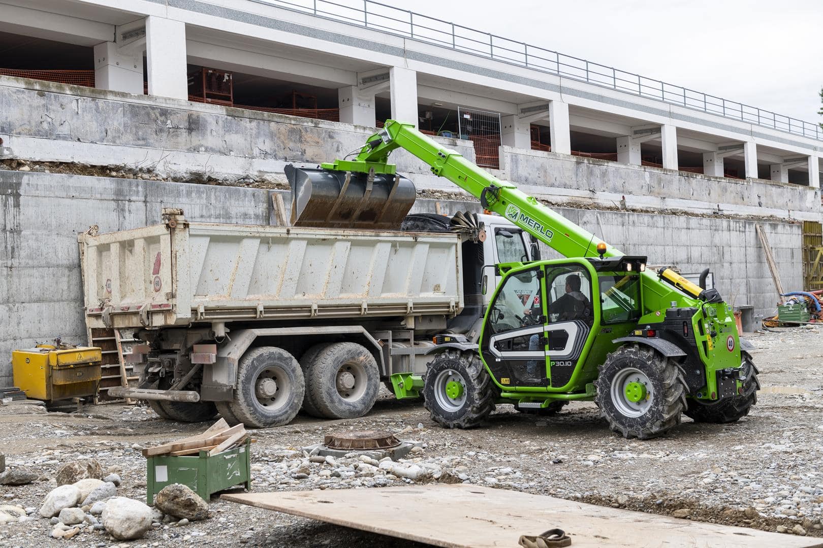 Merlo Panoramic 30.10 starre verreiker laadt een kiepwagen op bouwplaats